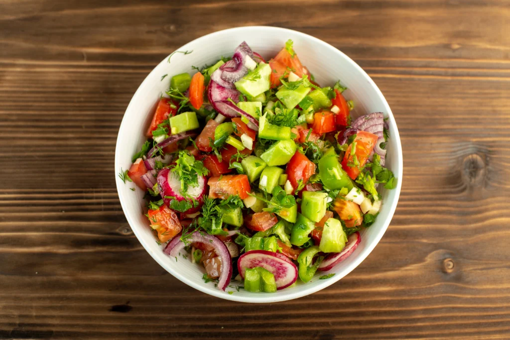 Fresh Shirazi Salad with diced cucumbers, tomatoes, and onions garnished with dried mint in a white bowl