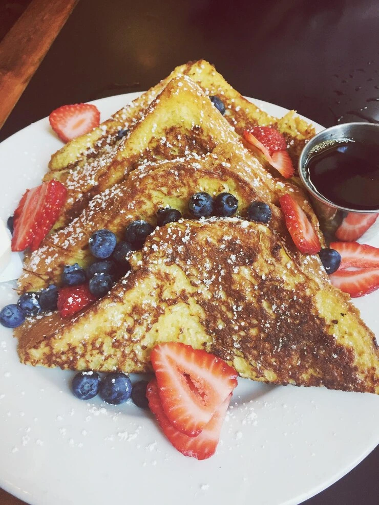Fluffy French toast slices on a white plate, topped with fresh berries and a drizzle of maple syrup, seasoned with McCormick vanilla and cinnamon.