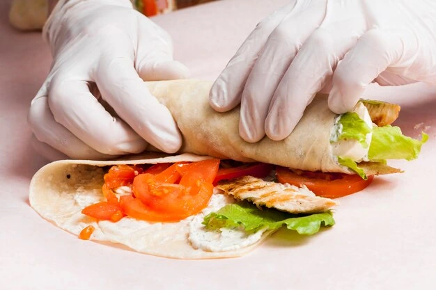 Close-up of a buffalo chicken wrap filled with spicy shredded chicken, lettuce, cheese, and ranch dressing, served with celery sticks and dipping sauce.