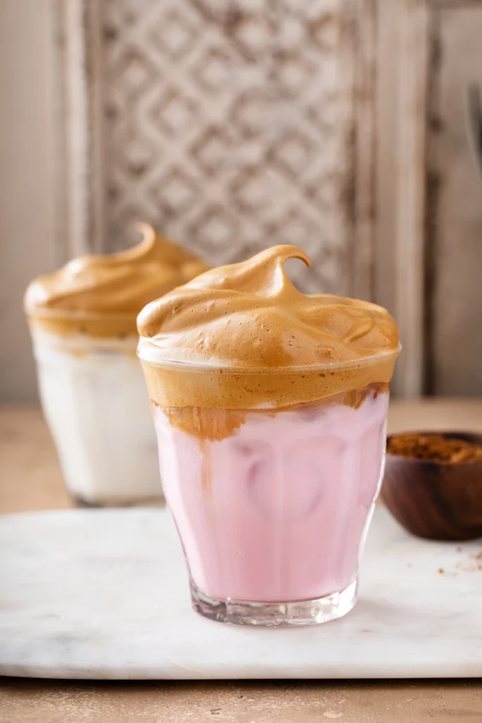 A glass of homemade Starbucks Pink Drink with fresh strawberries, ice, and a pink creamy base, served in a clear cup on a white marble counter.
