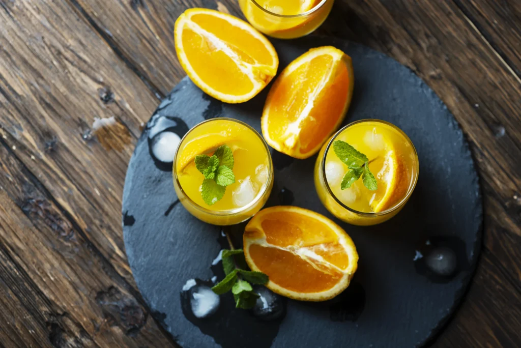 Freshly made Orange Crush cocktail with ice, orange slices, and a straw in a glass on a wooden table.