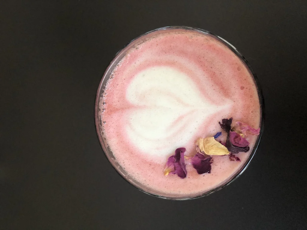 A glass of homemade Starbucks Pink Drink with fresh strawberries, ice, and a pink creamy base, served in a clear cup on a white marble counter