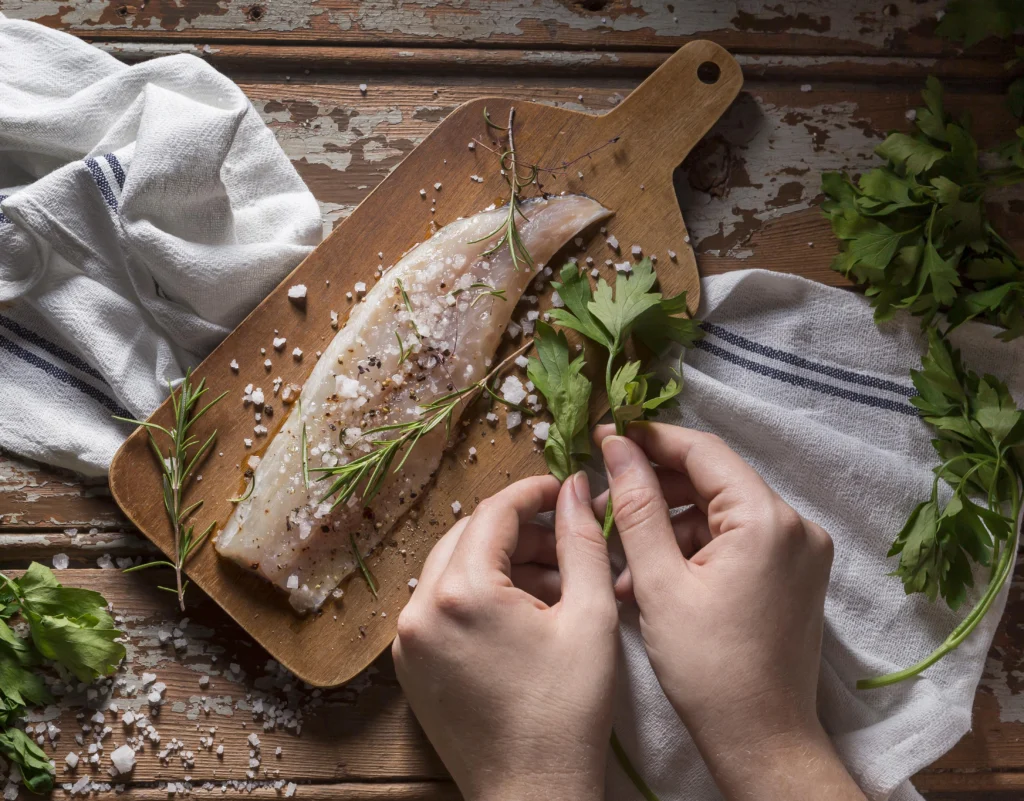 Pan-seared rockfish fillet served with lemon wedges and steamed vegetables on a white plate