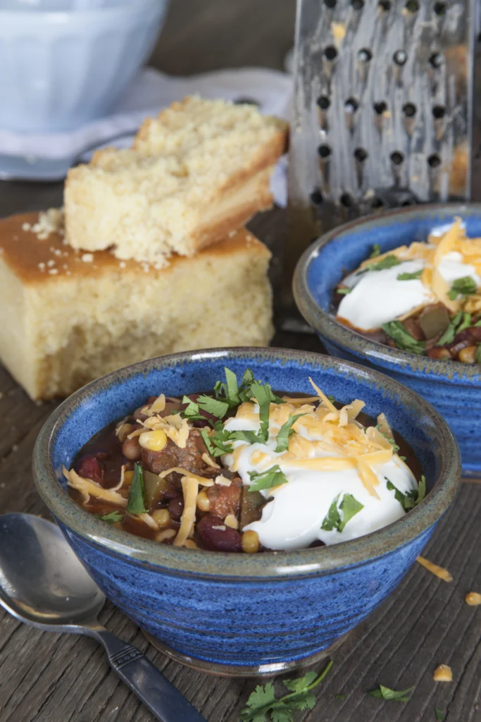 Bowl of authentic elk chili topped with fresh herbs and served with cornbread on the side