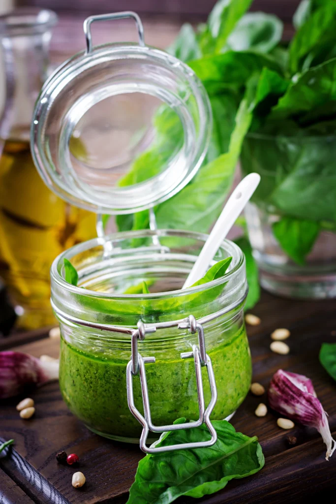 Nut-free basil pesto served in a glass jar with ingredients like basil leaves, garlic, and olive oil on a kitchen counter