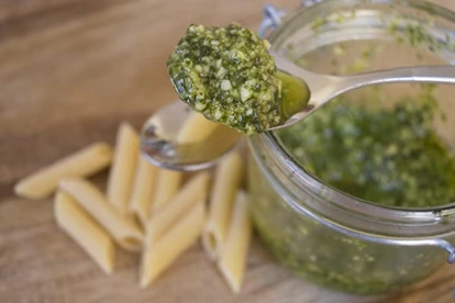 Nut-free basil pesto served in a glass jar with ingredients like basil leaves, garlic, and olive oil on a kitchen counter