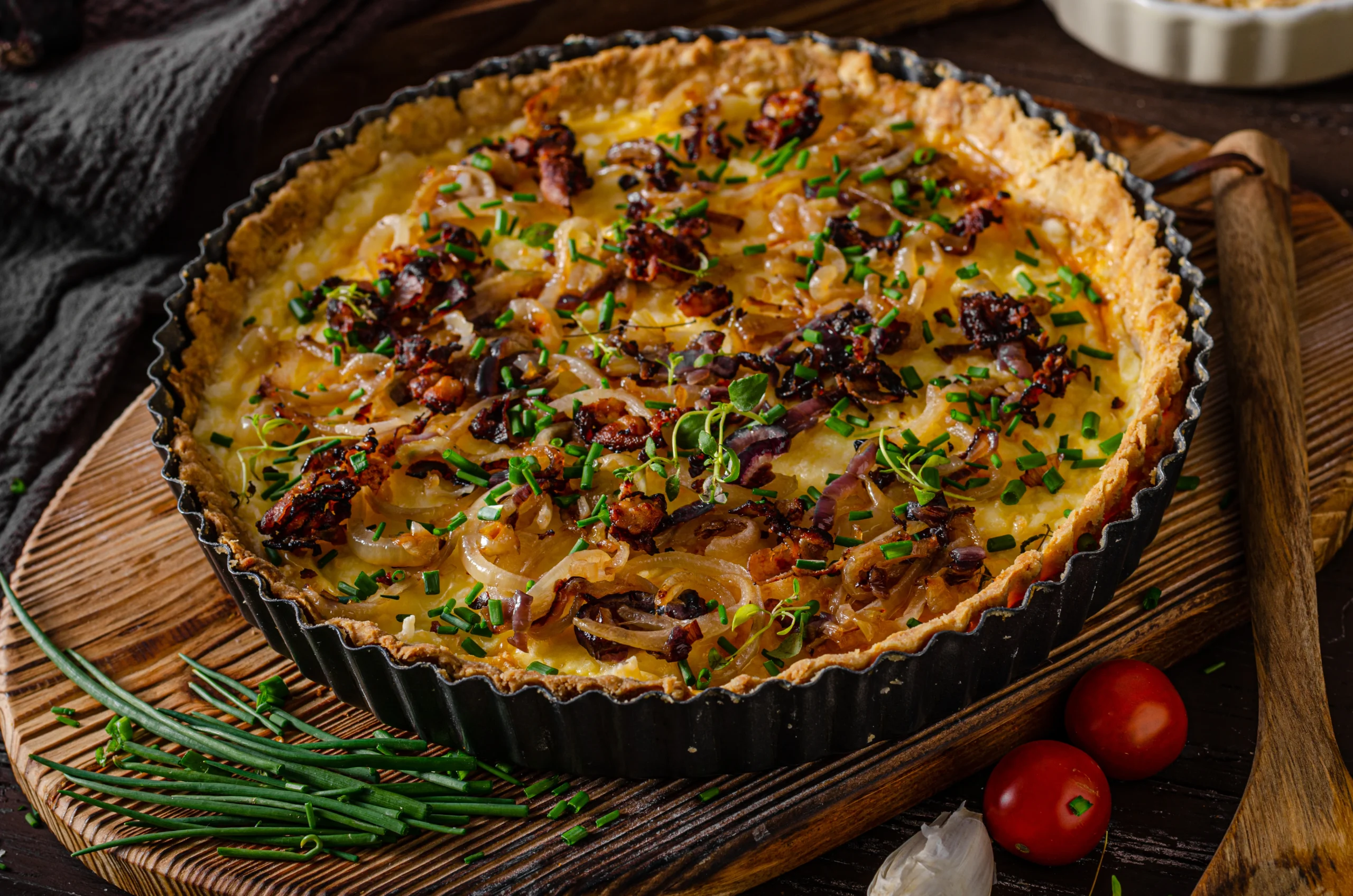 Crispy bacon savoury tart garnished with fresh herbs on a wooden board