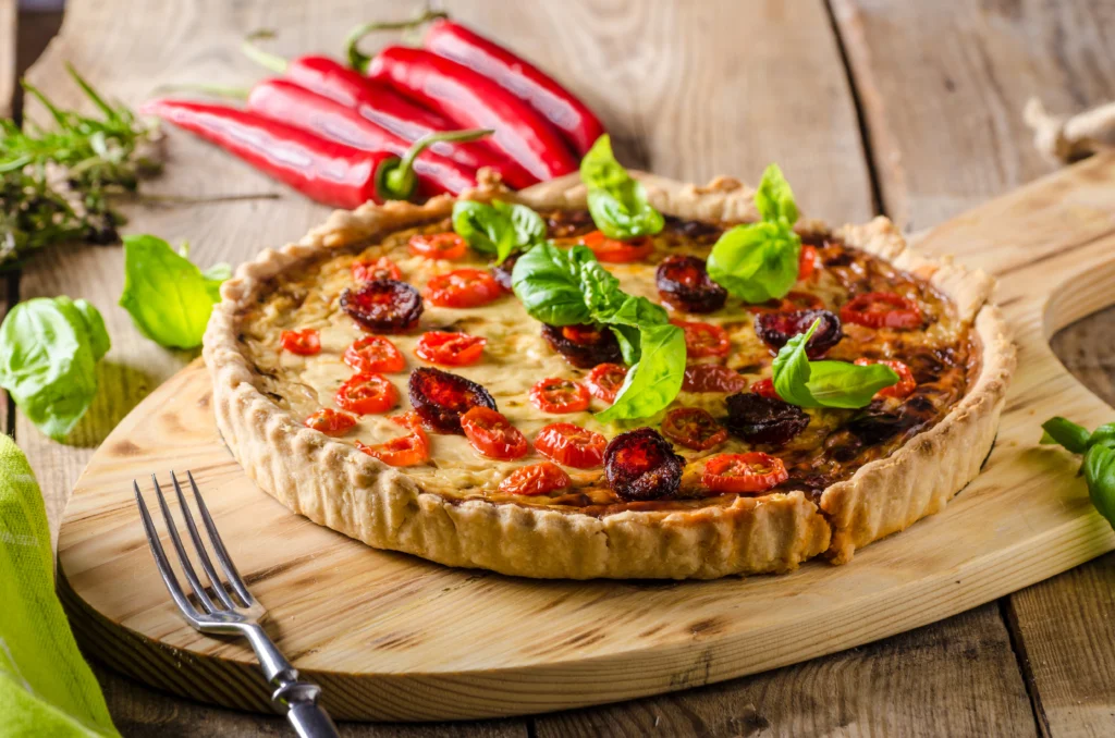 Crispy bacon savoury tart garnished with fresh herbs on a wooden board
