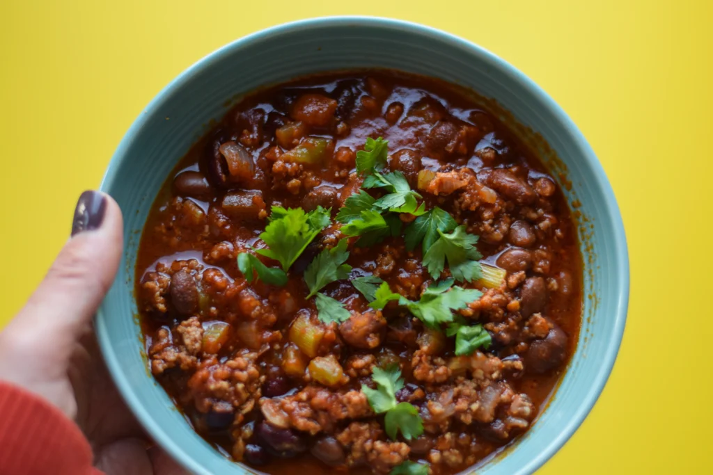 Freshly cooked bush beans served in a bowl with colorful vegetables and herbs on a wooden table.