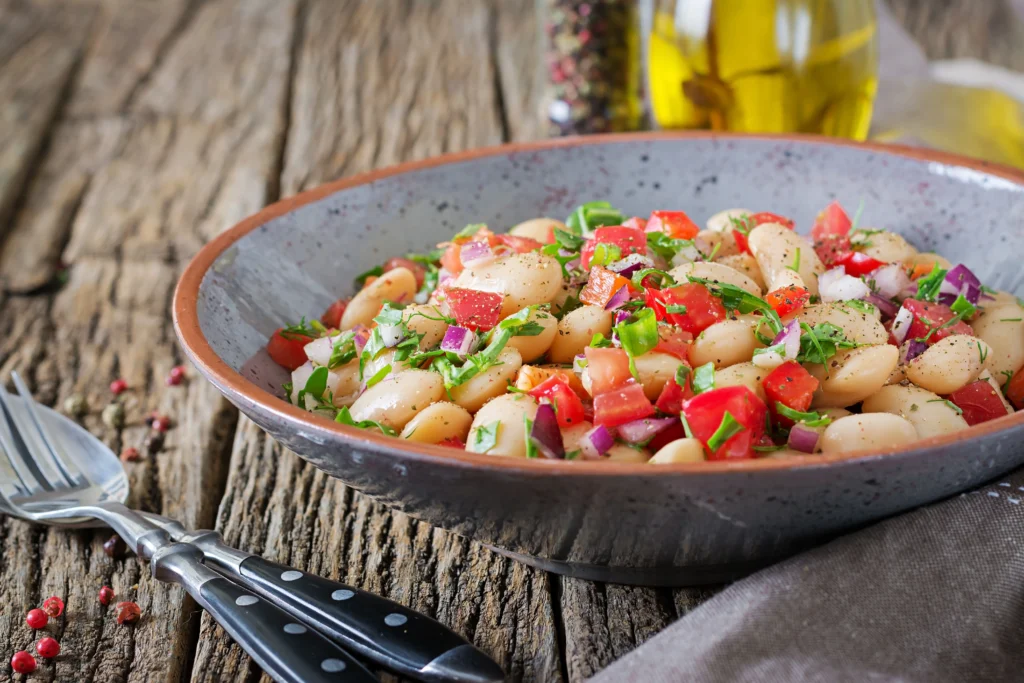 Freshly cooked bush beans served in a bowl with colorful vegetables and herbs on a wooden table.