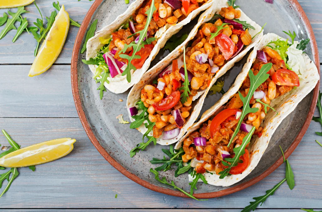 Freshly cooked bush beans served in a bowl with colorful vegetables and herbs on a wooden table.