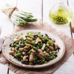 Freshly cooked bush beans served in a bowl with colorful vegetables and herbs on a wooden table.