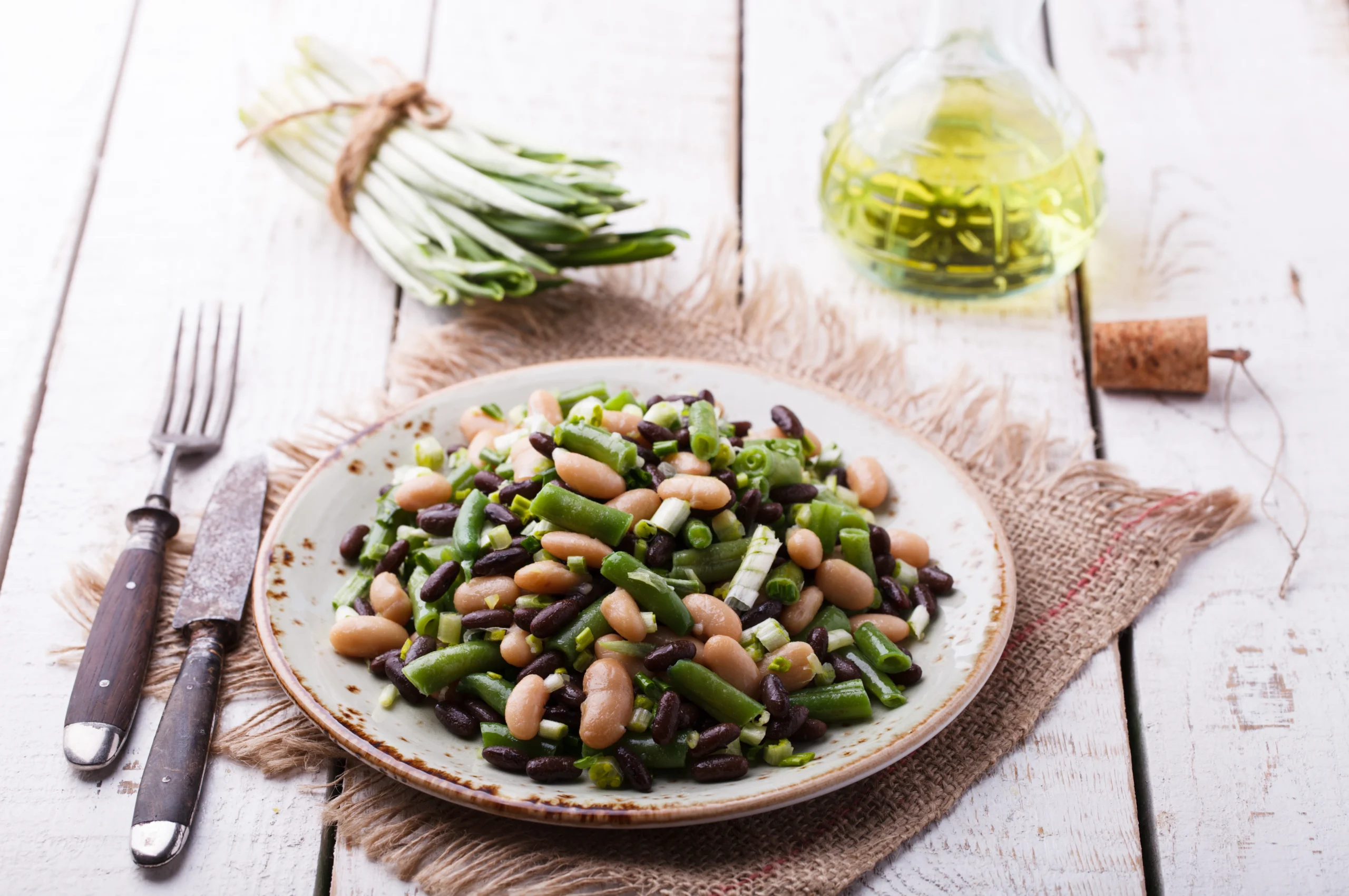 Freshly cooked bush beans served in a bowl with colorful vegetables and herbs on a wooden table.