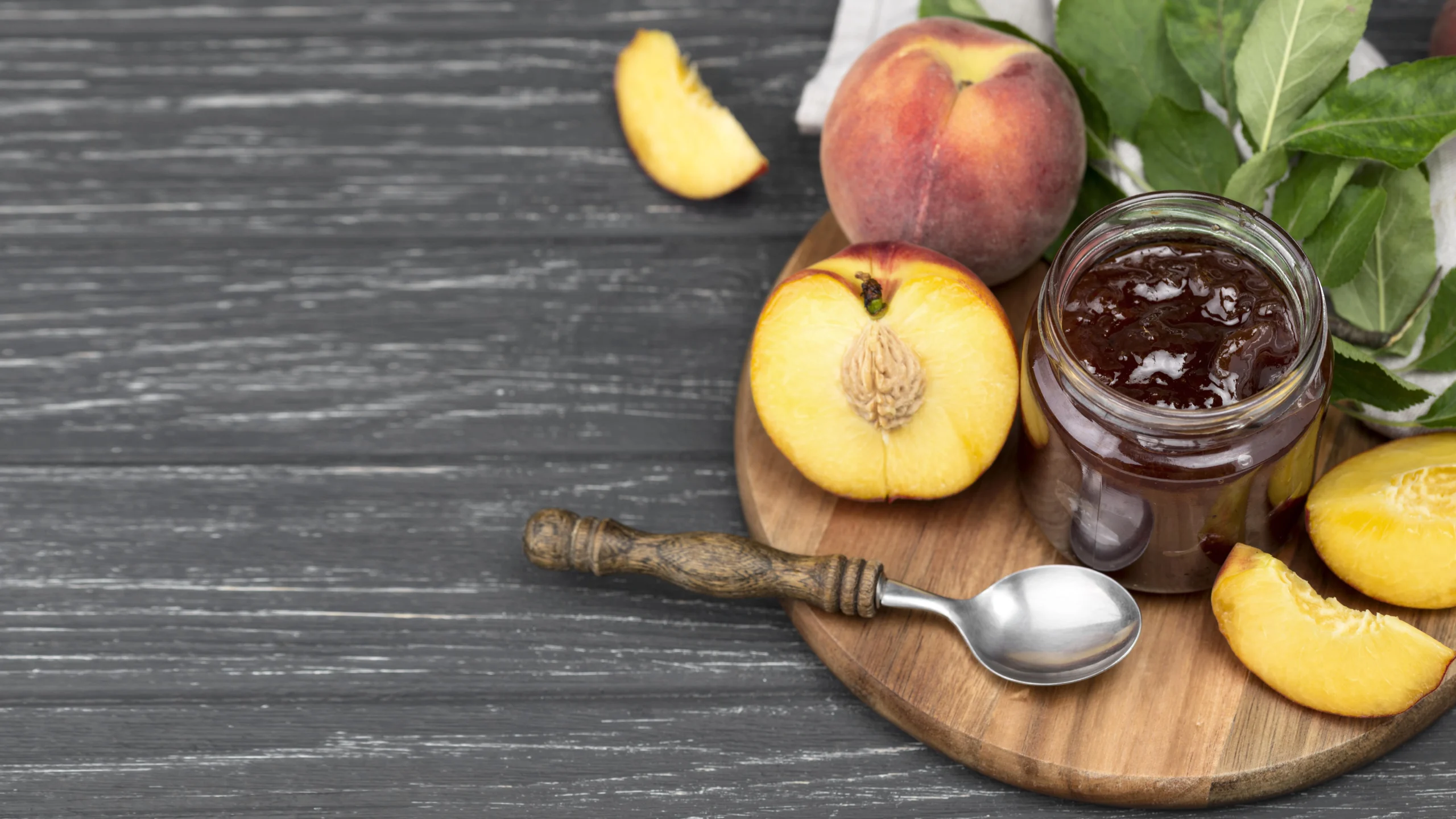 Homemade peach jam in a glass jar with fresh peaches on a wooden table