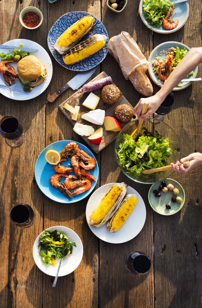 A close-up shot of a shrimp boil, featuring shrimp, corn, and potatoes, neatly arranged on a tray inside a red-and-white Igloo cooler. The cooler is lined with a checkered red-and-white cloth.