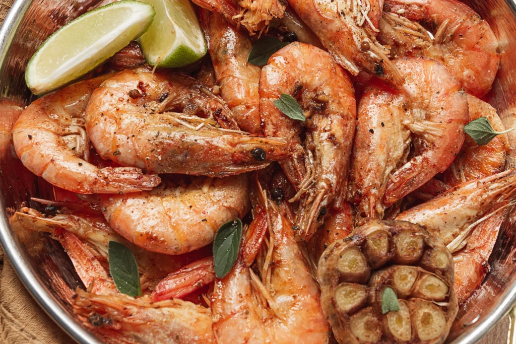 A close-up shot of a shrimp boil, featuring shrimp, corn, and potatoes, neatly arranged on a tray inside a red-and-white Igloo cooler. The cooler is lined with a checkered red-and-white cloth.