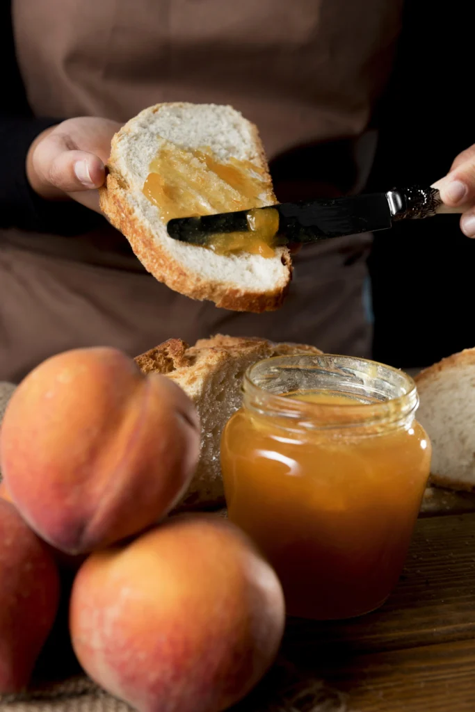 Homemade peach jam in a glass jar with fresh peaches on a wooden table.
