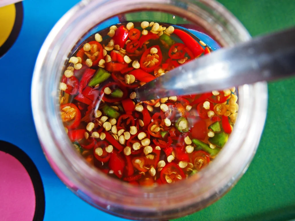 Homemade Tabasco sauce in a glass bottle with fresh red chili peppers and garlic on a wooden table.