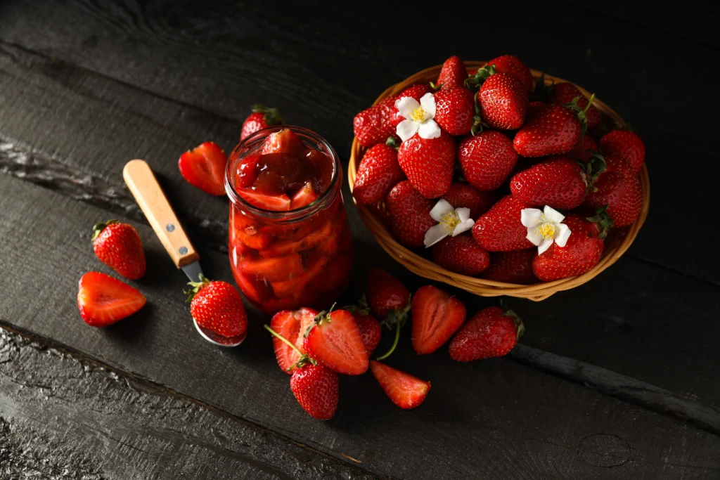Homemade strawberry preserves in glass jars with fresh strawberries on a wooden table