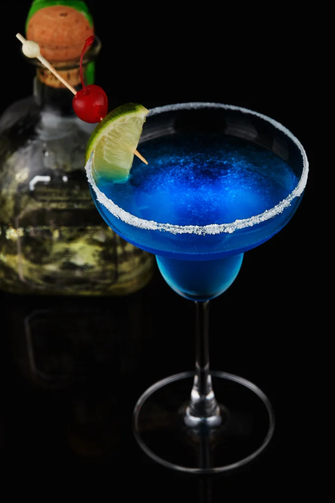 Blue Margarita cocktail in a glass with a lime wedge and blueberries, garnished with a salt rim, served on a summer night