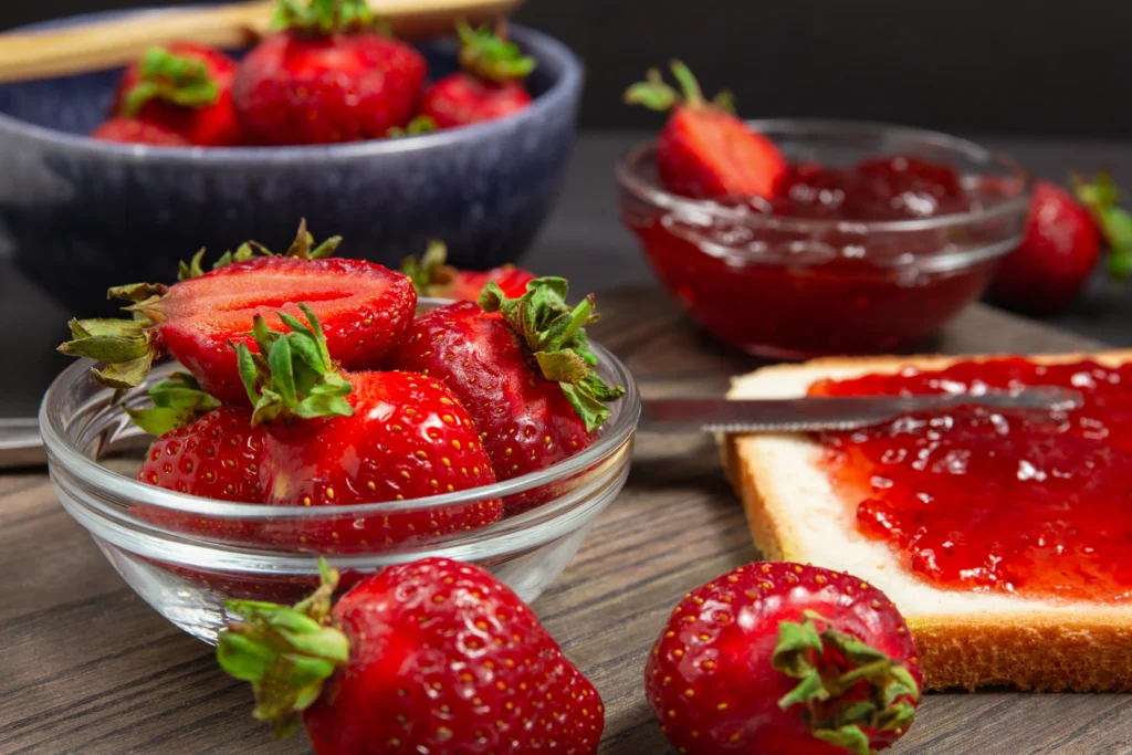 Homemade strawberry preserves in glass jars with fresh strawberries on a wooden table
