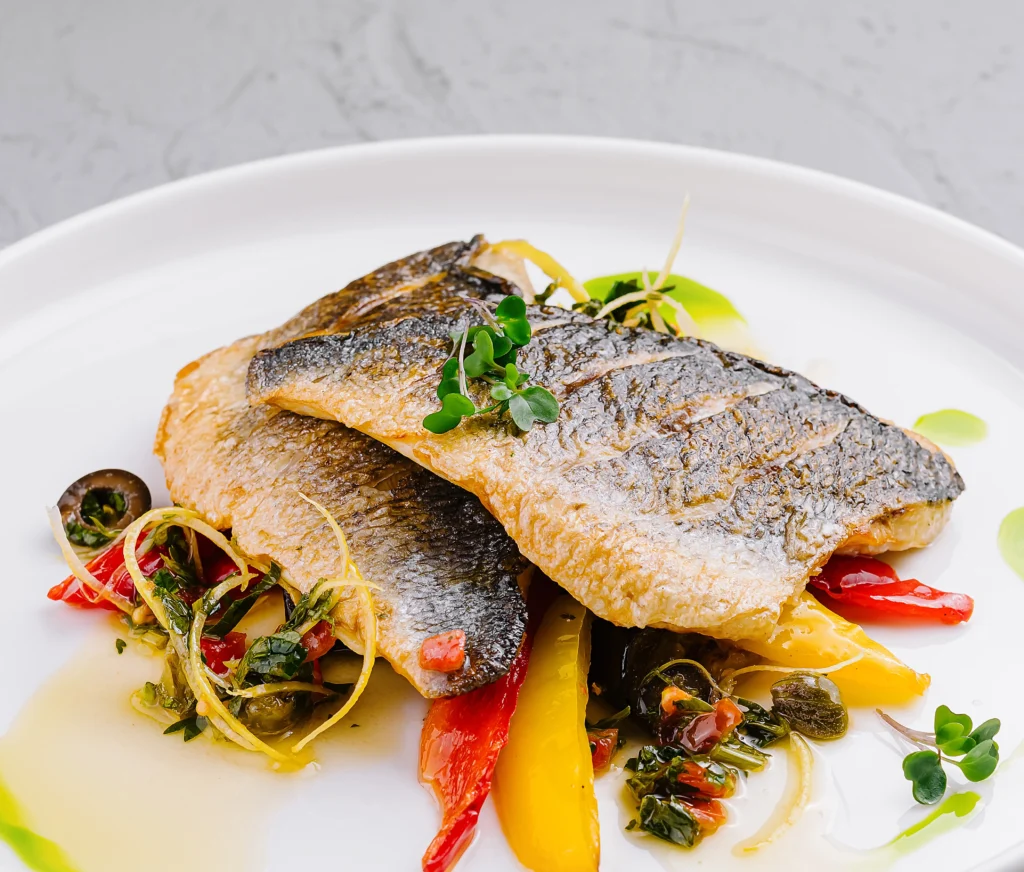 Grilled branzino fillet with garlic, olive oil, and lemon slices on a serving platter.