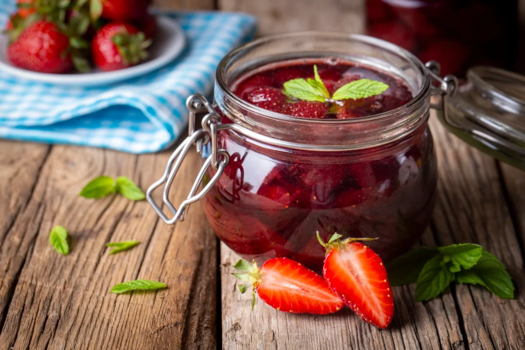 Homemade strawberry preserves in glass jars with fresh strawberries on a wooden table