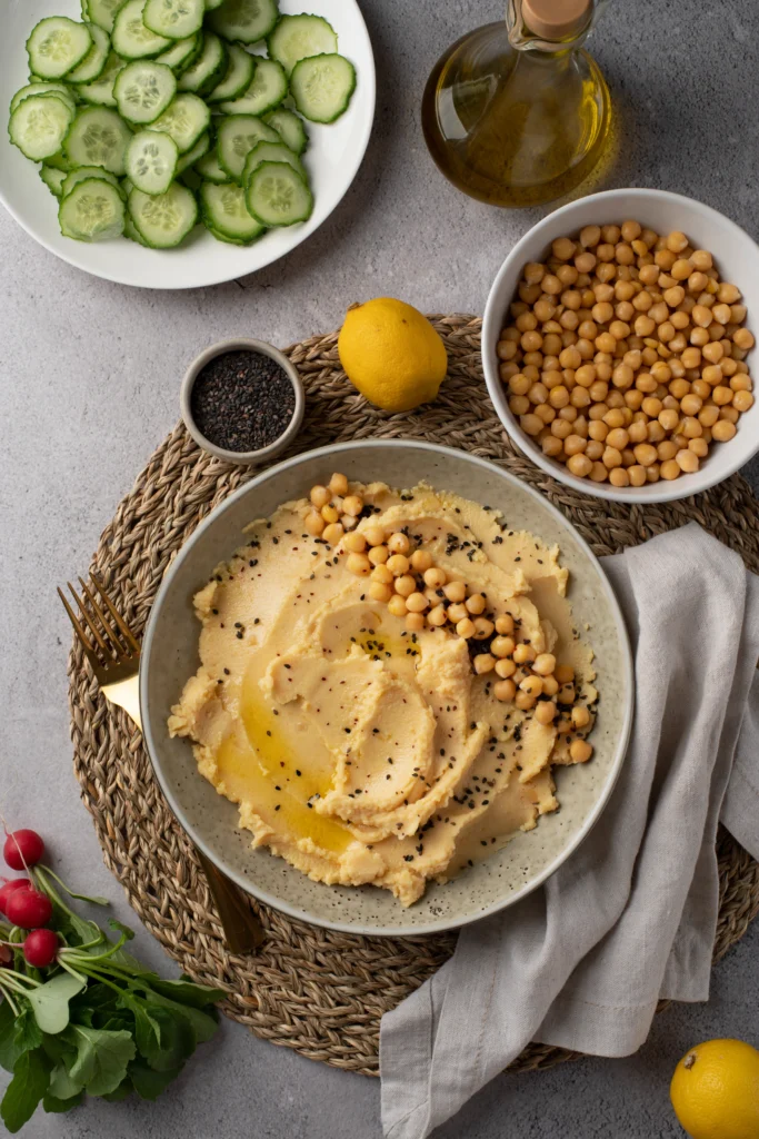 Bowl of creamy tahini-free hummus garnished with olive oil and paprika, served with fresh vegetables and pita bread