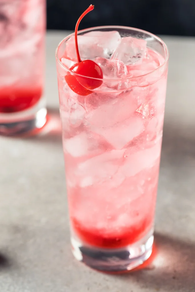 A refreshing Shirley Temple mocktail with ginger ale, grenadine, and a maraschino cherry served in a tall glass.
