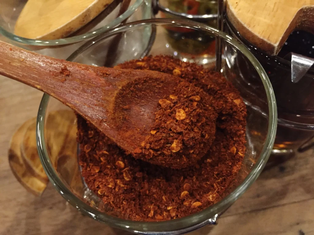 A bowl of homemade smoky chili seasoning blend with paprika, cumin, and chili powder on a rustic wooden table.