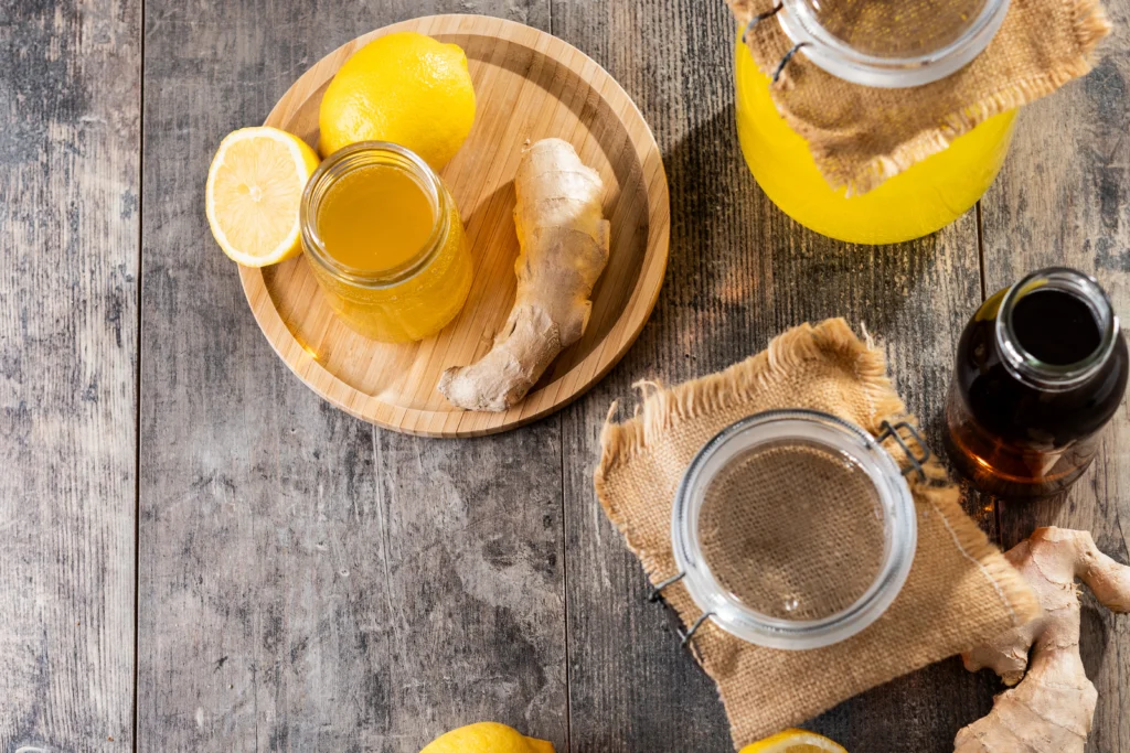 Active Ginger Bug in a glass jar with bubbles, cloth cover, and fresh ginger and sugar on a wooden countertop
