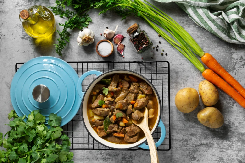 A glass jar filled with golden bone broth next to a slow cooker, surrounded by fresh herbs and vegetables.