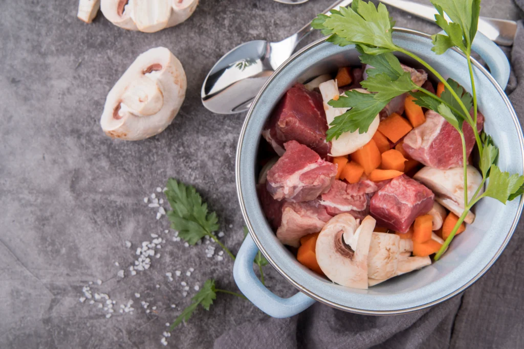 A glass jar filled with golden bone broth next to a slow cooker, surrounded by fresh herbs and vegetables.