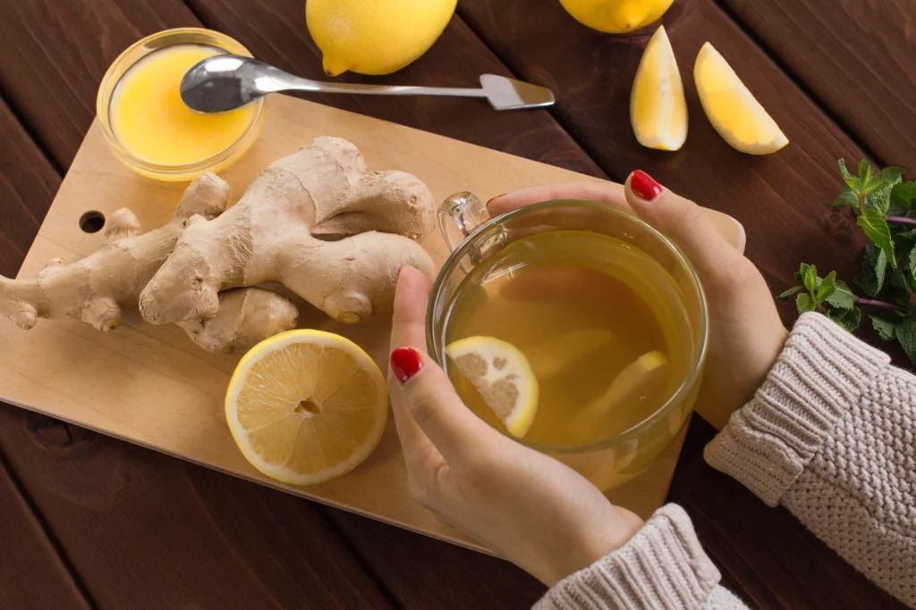 Active Ginger Bug in a glass jar with bubbles, cloth cover, and fresh ginger and sugar on a wooden countertop