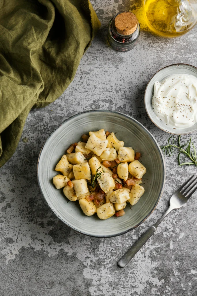 A rustic plate filled with crispy mashed potato cakes, garnished with fresh herbs, served with a small bowl of sour cream on a wooden table, showcasing creative ways to use leftover mashed potatoes.
