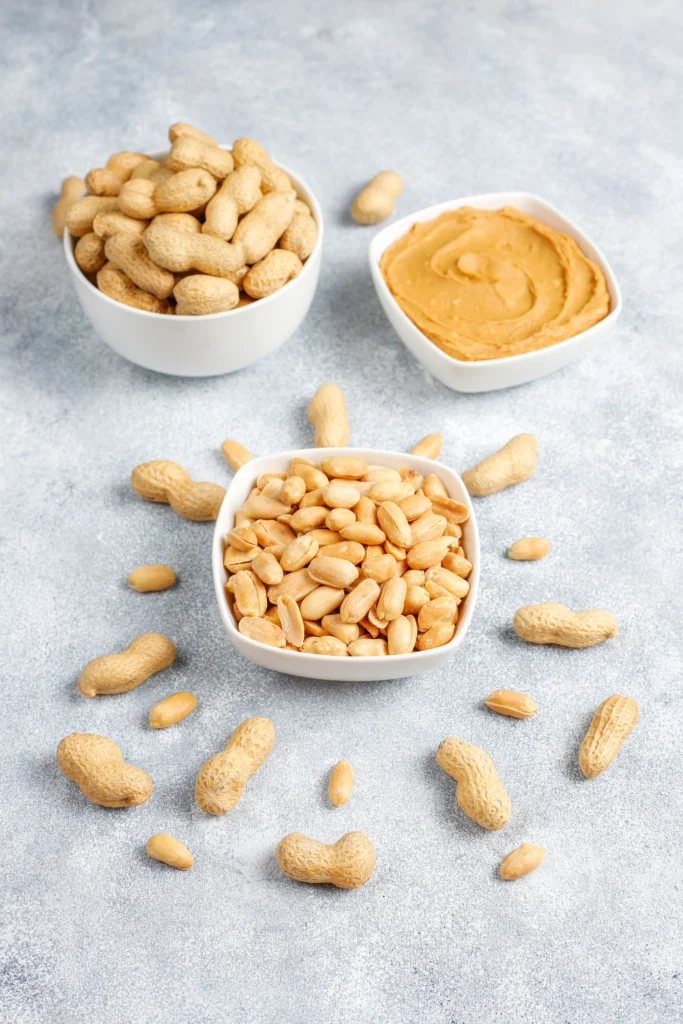 Bowl of creamy homemade peanut sauce with a spoon, surrounded by peanuts, lime, and fresh herbs.