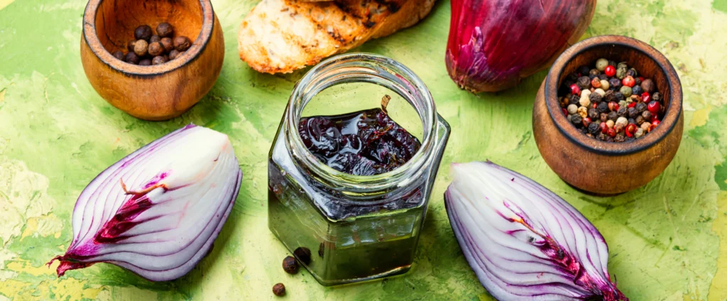 Homemade pickled red onions in a glass jar with vinegar, peppercorns, and garlic on a kitchen counter.
