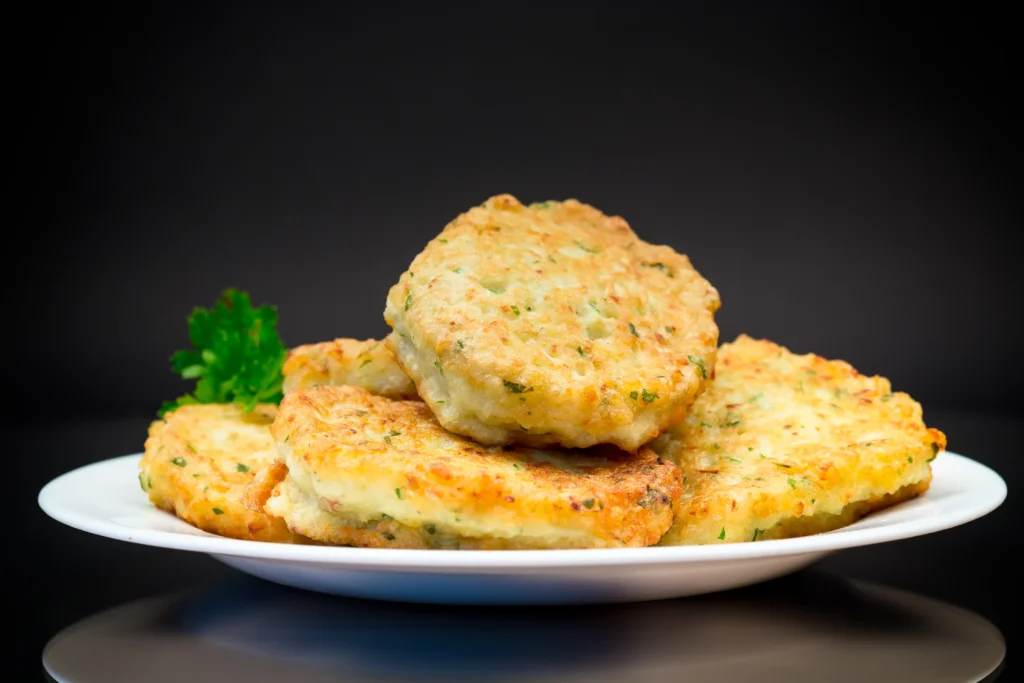 A rustic plate filled with crispy mashed potato cakes, garnished with fresh herbs, served with a small bowl of sour cream on a wooden table, showcasing creative ways to use leftover mashed potatoes.