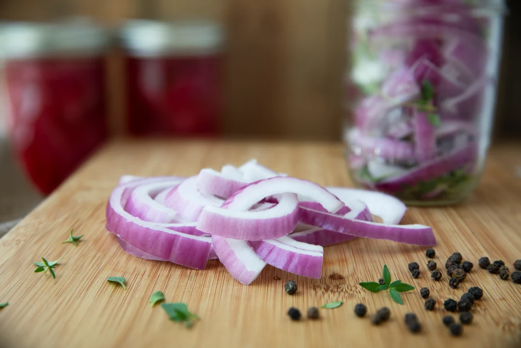 Homemade pickled red onions in a glass jar with vinegar, peppercorns, and garlic on a kitchen counter.