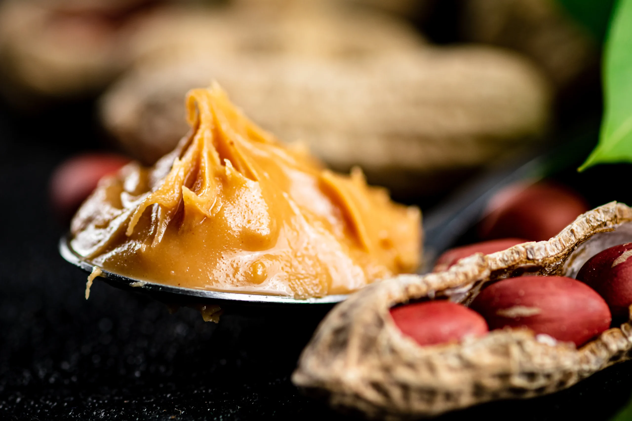 Bowl of creamy homemade peanut sauce with a spoon, surrounded by peanuts, lime, and fresh herbs.