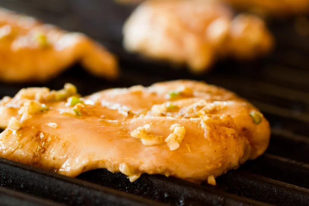 Almond chicken glazed with honey sauce, garnished with toasted almonds and fresh herbs on a white plate.
