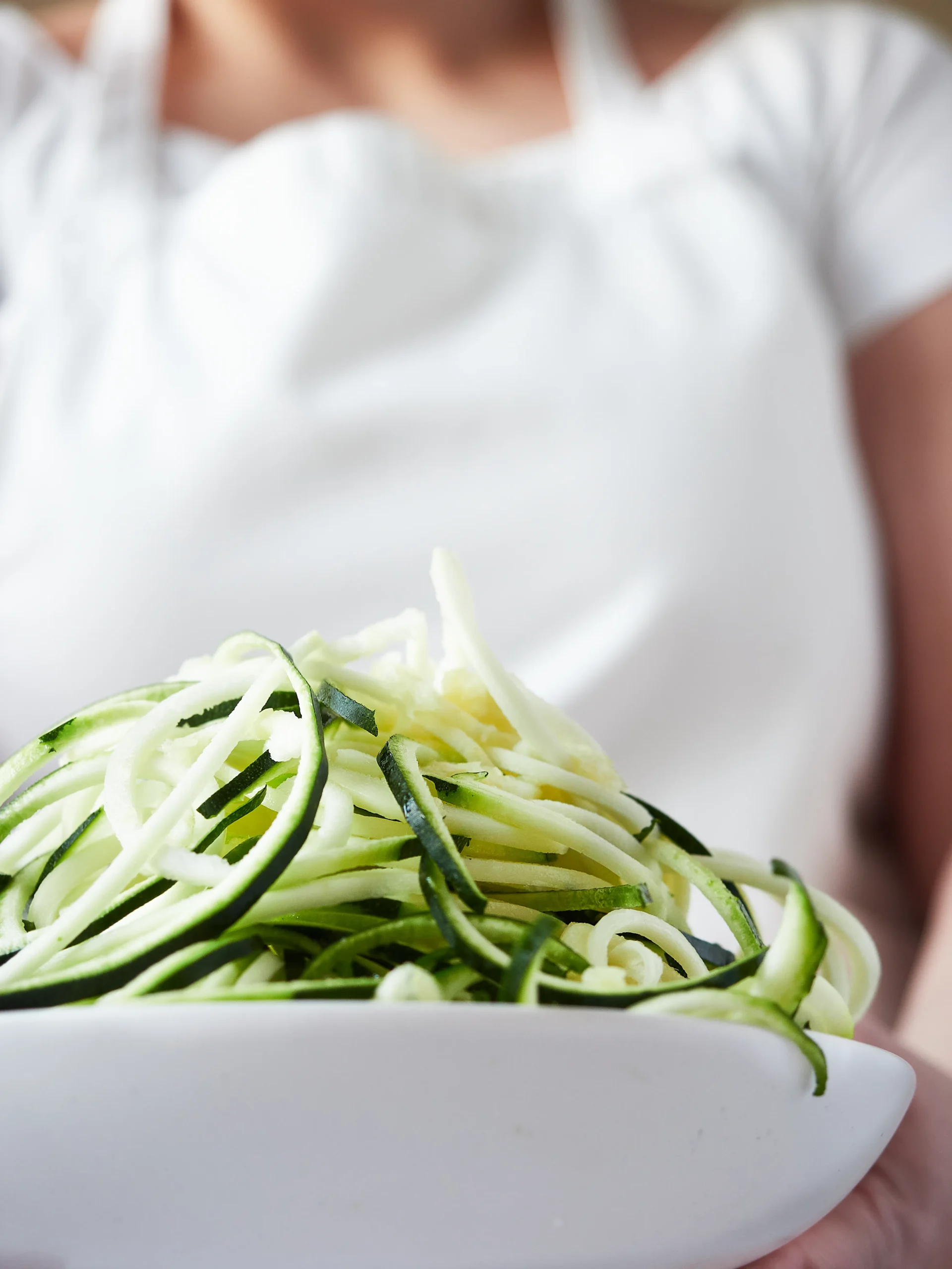 Zucchini noodles tossed with cherry tomatoes and green pesto, served in a white bowl.