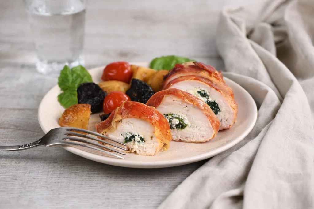 Oven-baked Caprese stuffed chicken breast filled with melted mozzarella, fresh basil, and tomatoes, drizzled with balsamic glaze on a white plate.