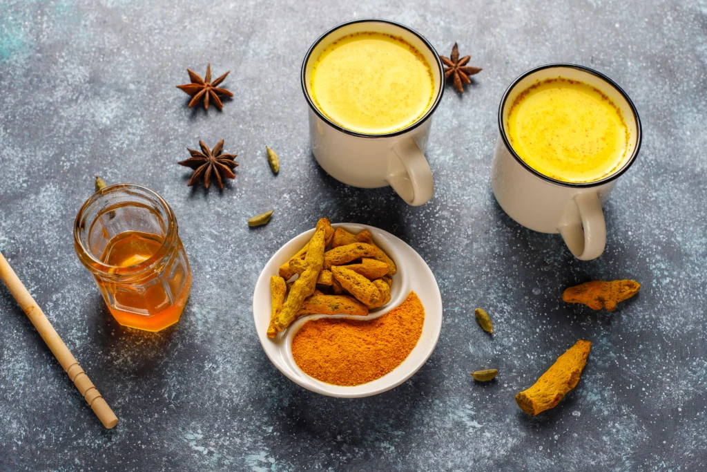 Spiced Golden Turmeric Latte in a ceramic mug with cinnamon sticks and fresh turmeric on a wooden table