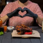 Spicy rib rub seasoning blend being sprinkled over raw pork ribs before grilling