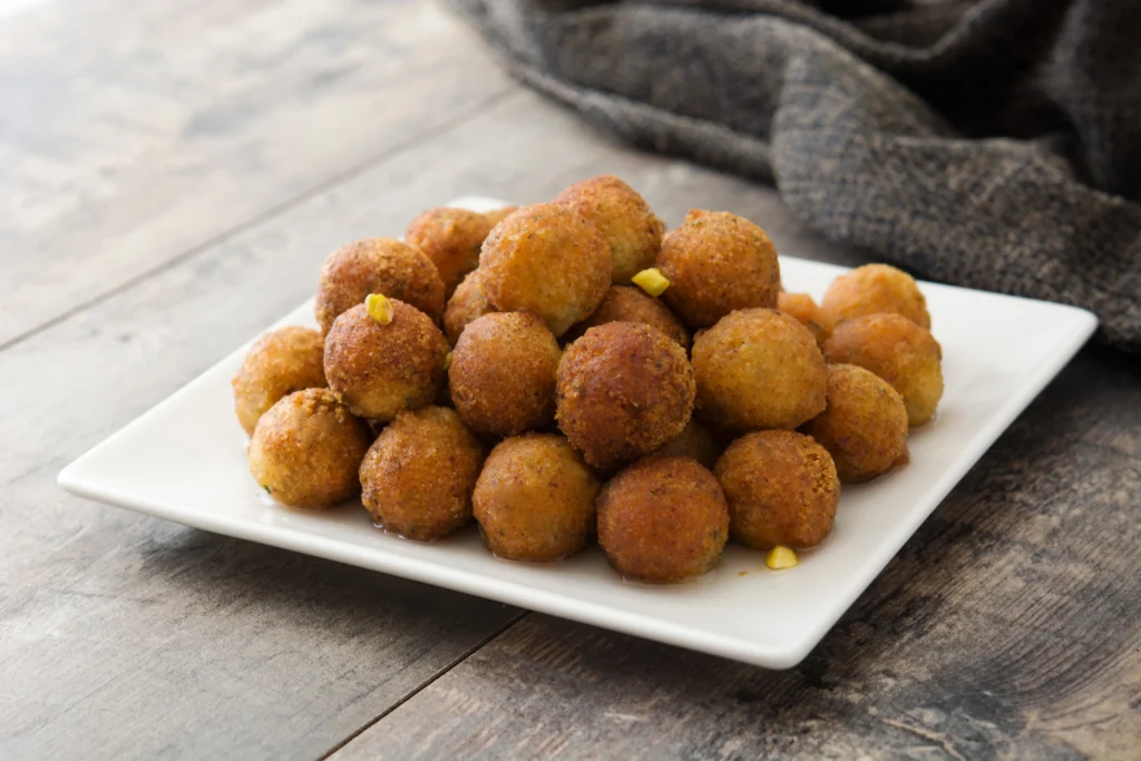 Golden crispy hush puppies served hot with fried fish and lemon wedges on a rustic plate