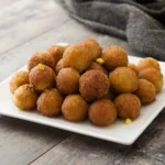 Golden crispy hush puppies served hot with fried fish and lemon wedges on a rustic plate