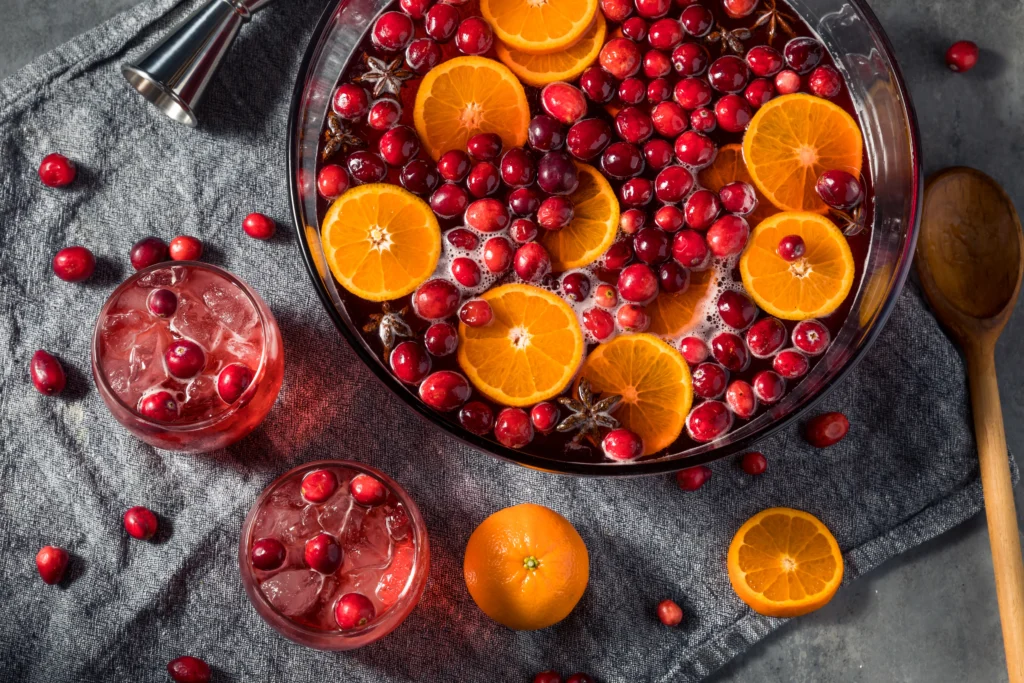 Colorful holiday rum punch cocktail with citrus slices, cranberries, and ice in a festive glass