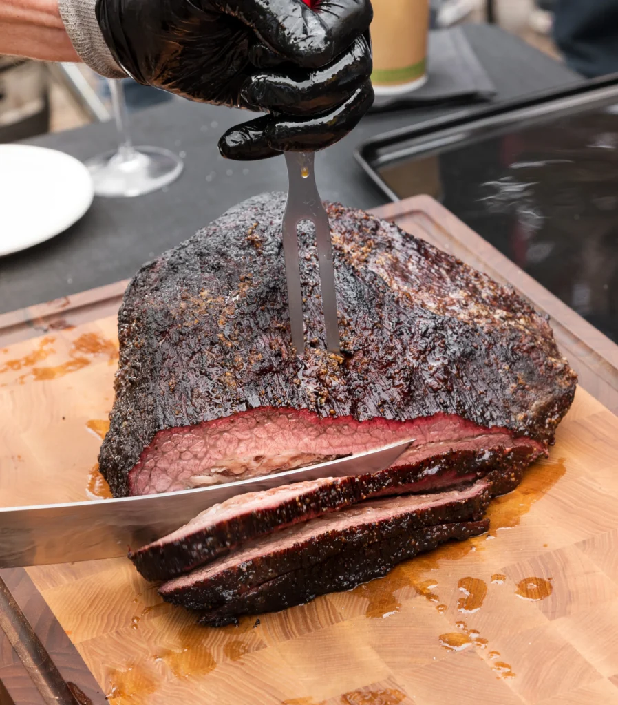 Smoked brisket sliced on a wooden board with a crispy bark and juicy interior, served at a BBQ party