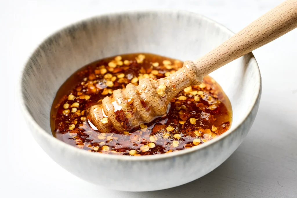 Jar of homemade spicy hot honey being drizzled over crispy fried chicken on a wooden table